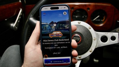 Hand met een mobiele telefoon waarop de nieuwe website te zien is met op de achtergrond het dashboard van een classic Mini