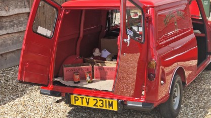 Een Mini Van van de Britse Royal Mail van achter bezien, met de laaddeuren open. Er zijn enkele dozen met opschrift "Post Office" en een Postman Pat pop te zien.